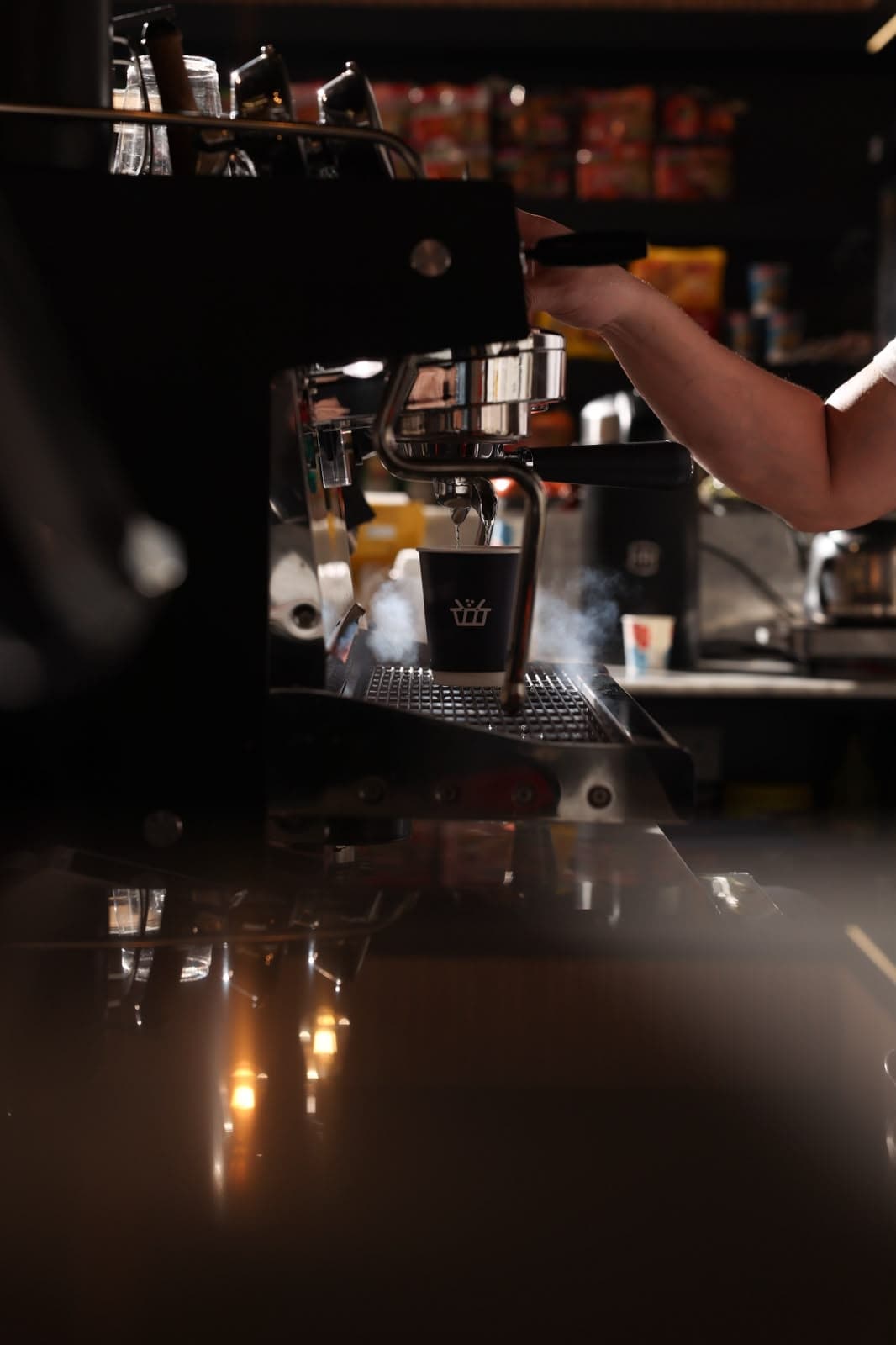 A Sella-branded cup filling under an espresso machine, steam rising, a barista's hand on the portafilter